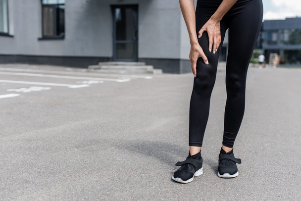partial view of sportswoman in black sneakers with leg pain on street - Foto, immagini
