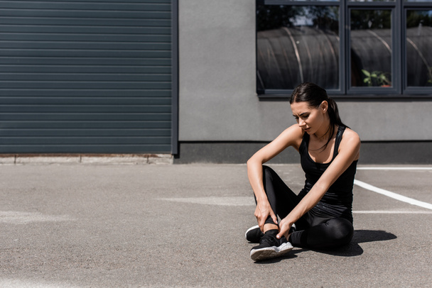 sportswoman in black sneakers with ankle pain on street - Foto, Imagem