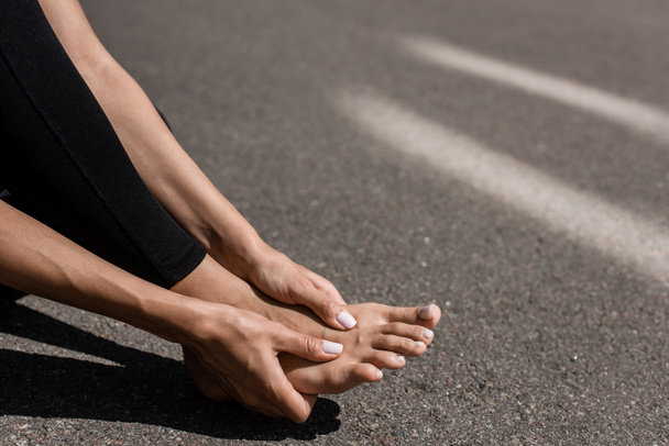 partial view of barefoot sportswoman with foot pain on street - Foto, Bild