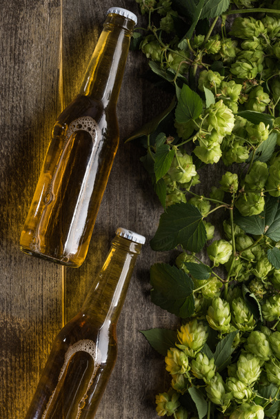 top view of beer in bottles near green hop on wooden background - Fotó, kép