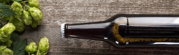 vista superior de cerveja em garrafa marrom com salto verde sobre fundo de madeira, tiro panorâmico
 - Foto, Imagem