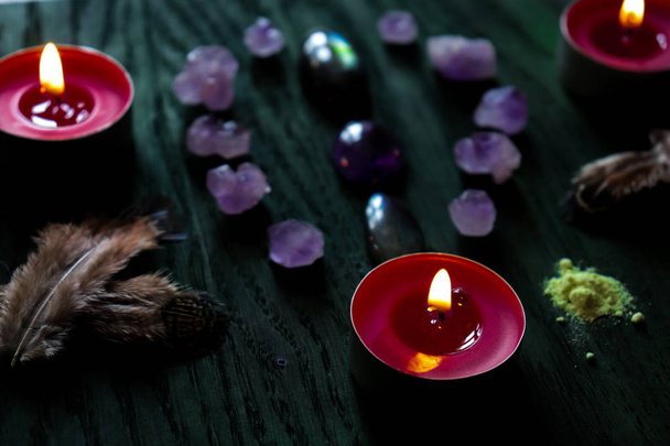 Aménagement magique de pierres (labradorite, améthyste), plumes, soufre et bougies rouges sur fond de bois vert
. - Photo, image