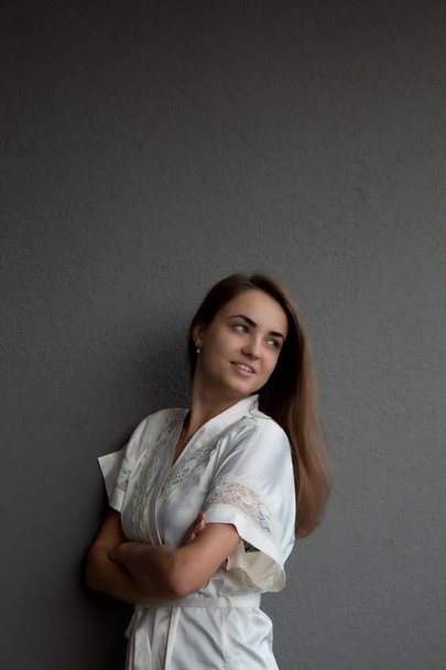 A young, beautiful girl with long brown hair in a white robe. Grey background. At the top of the image is space for text or graphics. - Photo, Image