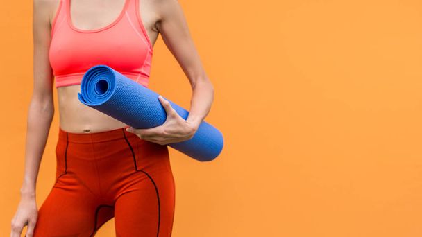 Sporty yoga girl with yoga mat wearing sport clothes over orange background - Фото, изображение