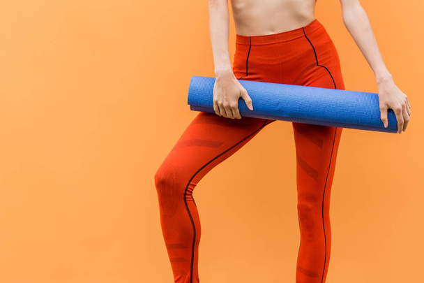 Sporty yoga girl with yoga mat wearing sport clothes over orange background - Foto, Imagen
