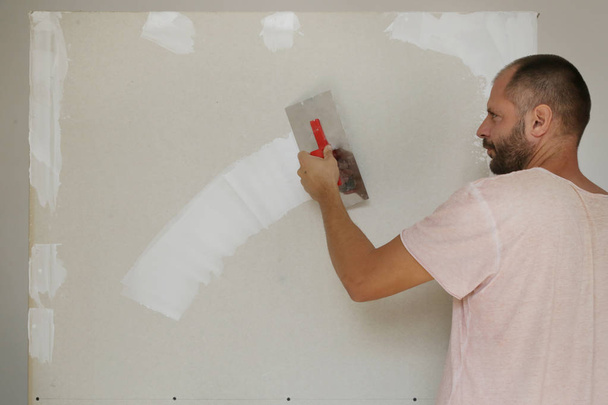 Hombre enyesando la pared con masilla-cuchillo. Fijación de la superficie de la pared y preparación para la pintura. Proyecto de mejora de viviendas DIY
. - Foto, imagen