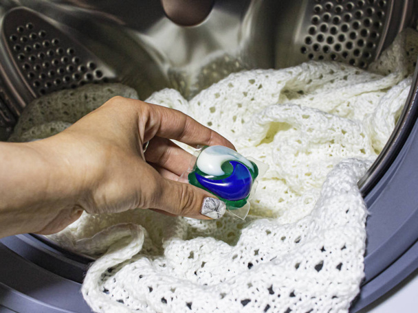 Dívčí ruka vytváří kapsli s práškem na mytí bílých věcí. - Fotografie, Obrázek