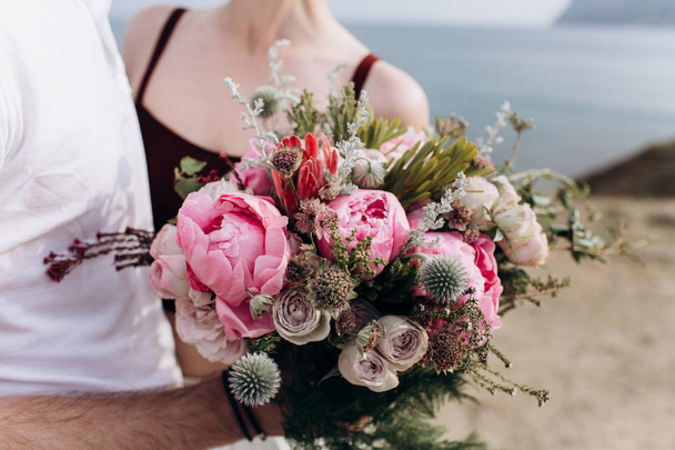 Pink wedding bouquet with a stone rose and peonies on the background of the sea. - Foto, afbeelding