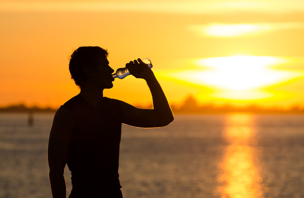 człowiek do picia butelka wody na plaży na wschód - Zdjęcie, obraz