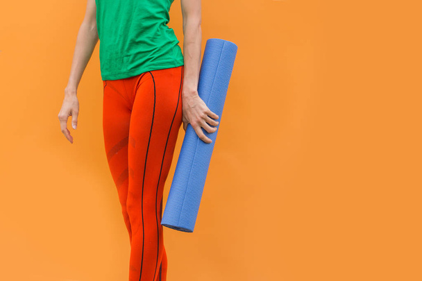 Sporty yoga girl with yoga mat wearing sport clothes over orange background - Photo, image