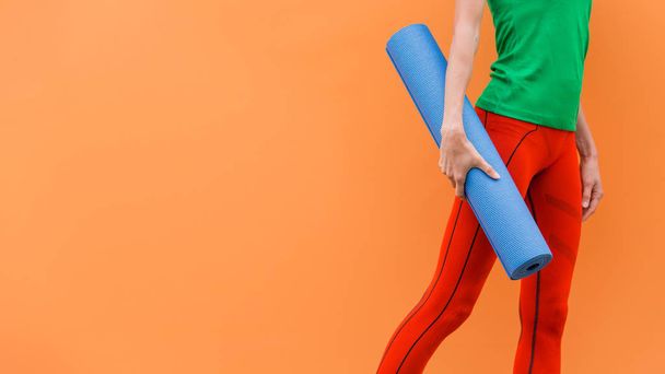 Sporty yoga girl with yoga mat wearing sport clothes over orange background - Foto, imagen