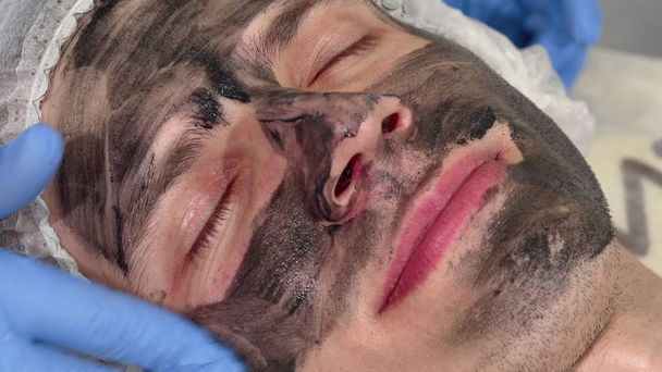 Beautician applying black mask on face of male client - Фото, зображення