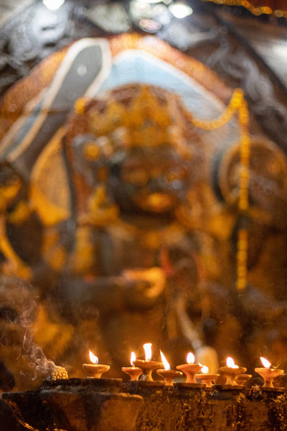 Statue of Kaal Bhairav with butterlamps on foreground. Selective focus, focus on butter lamps - Photo, Image