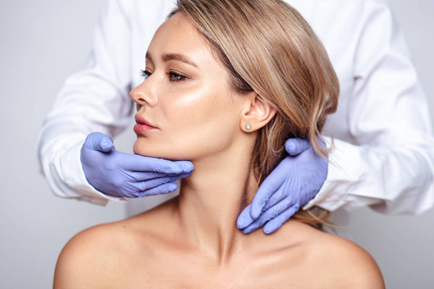 Close up portrait of young blonde woman with cosmetologyst hands in a gloves. Preparation for operation or procedure. Perfect skin, spa and care - Foto, immagini