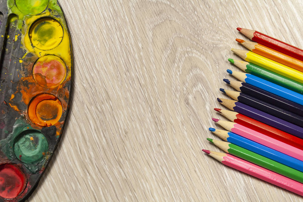 veelkleurige potloden en aquarel verven liggen op een tafel - Foto, afbeelding