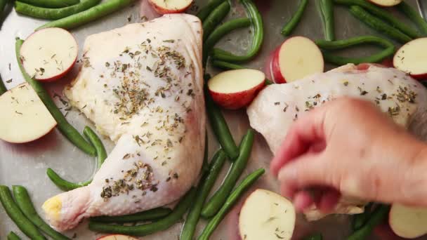 A woman puts dried herbs  and lemon slices on chicken quarter sheet pan dinner with potatoes and green beans - Footage, Video