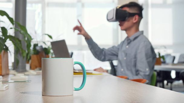 テーブルの上にコーヒーのカップ、バックグラウンドで仕事で3D VRメガネを使用している男 - 写真・画像