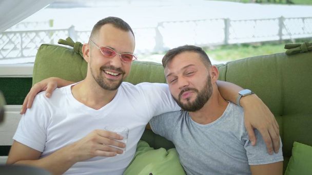 Gay couple smokes a hookah, sitting in the gazebo on the street on a sunny summer day. - 写真・画像