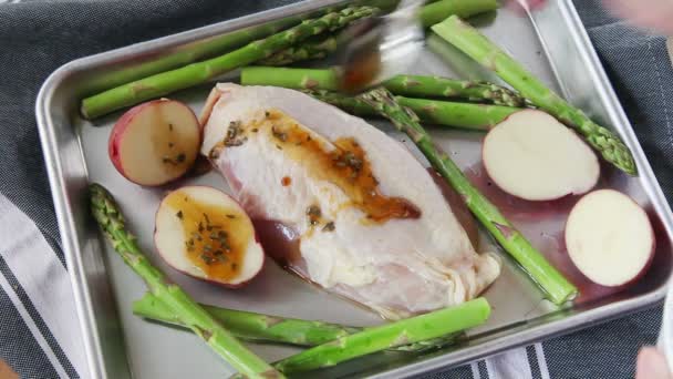 A woman adds a sauce to a chicken sheet pan dinner with asparagus and potatoes - Footage, Video