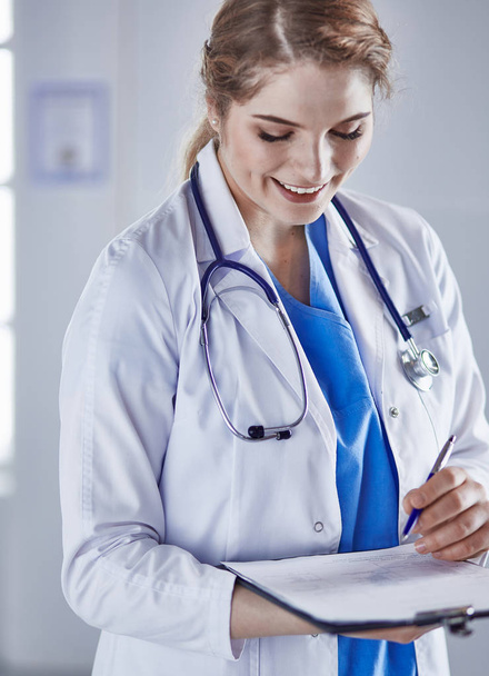 Mujer joven médico está de pie con tablero con portapapeles smilin
 - Foto, imagen