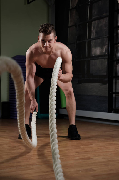 Muscular man with battle rope doing exercise in functional training gym - 写真・画像