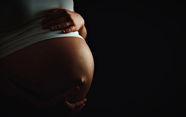 Bauch der schwangeren Frau einfarbig auf dunklem Hintergrund - Foto, Bild