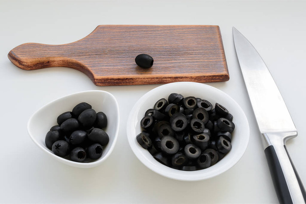 Sliced olives and whole black olives in a white bowls - Фото, изображение
