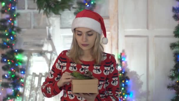 Portrait Of Women In Santa Hat Is Opening Present Box. Christmas Tree Is On. - Кадри, відео
