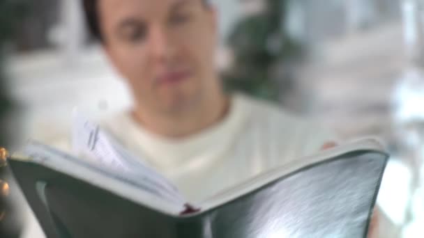 Young Man Reading Aloud From A Book Standing Next To The Christmas Tree. - Filmmaterial, Video