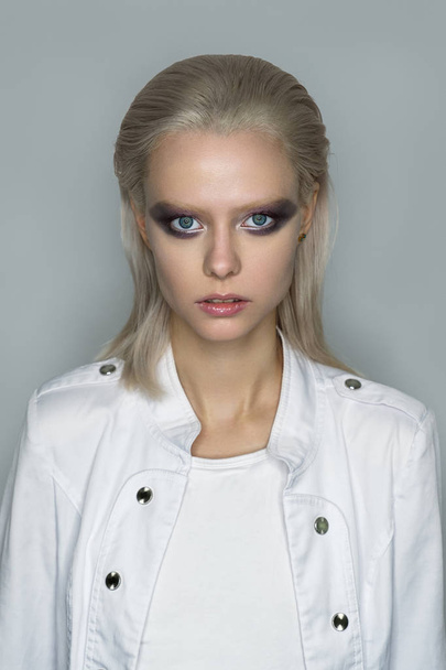 Portrait of a platinum blonde in white clothes with bright eye makeup in purple tones with a metallic glow. - Foto, Imagen