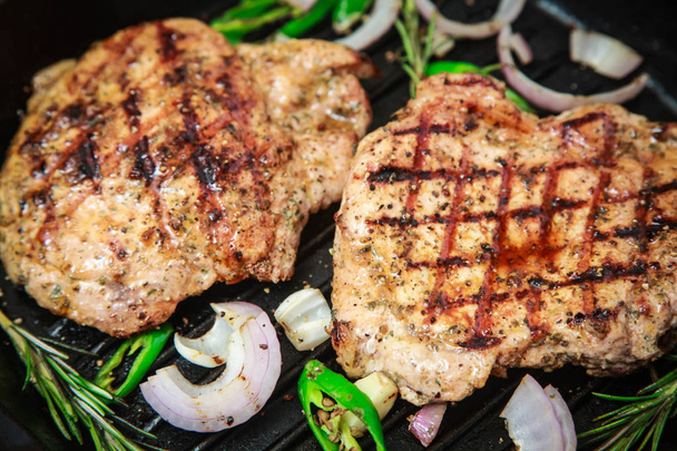 Geroosterde varkensvlees steak in een pan met hete groene peper en UI op een donkere achtergrond. - Foto, afbeelding