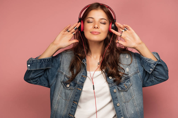 A beautiful girl in a jeans listens to music pretty smiling, putting her hands on the headphones. - Φωτογραφία, εικόνα