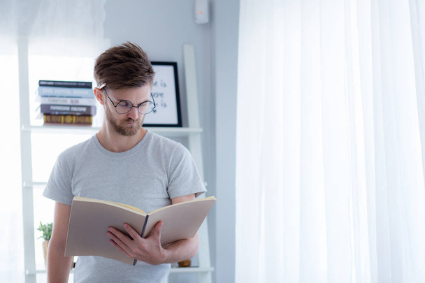 Handsome guy in eyeglasses is reading book preparing exam with s - Photo, image