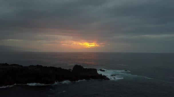 Lassú repülés felett viharos óceán felé gyönyörű színes naplemente. Légi drone lövés óceán hullámai borulás fekete sziklák. - Felvétel, videó
