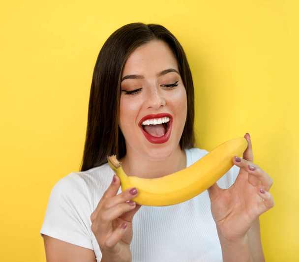 woman holding banana on yellow background - Фото, изображение