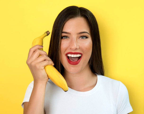 young woman holding banana on yellow background - Valokuva, kuva