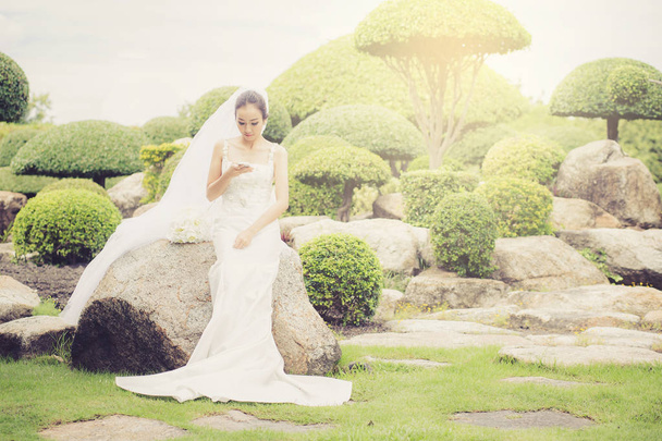 bride touch on phone in wedding dress on garden. - Fotografie, Obrázek