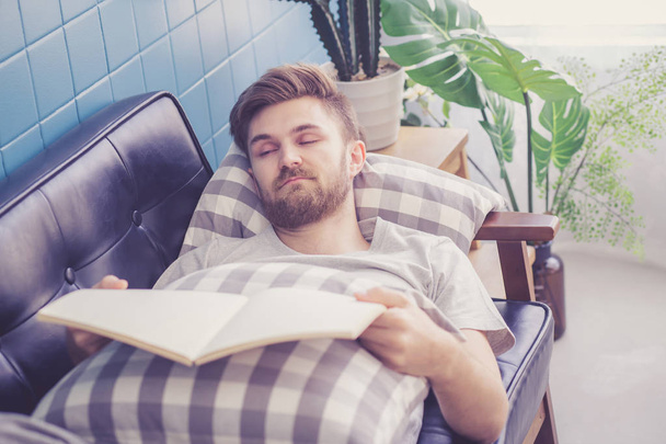 Человек читает книгу, держа руку спать на диване
. - Фото, изображение