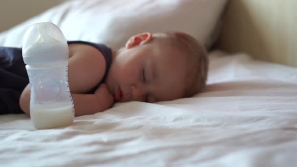 Carino bambino che dorme in un grande letto vicino a una bottiglia con latte al rallentatore
 - Filmati, video