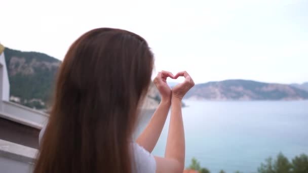 A lány egy szív alakú a kezét a háttérben a tenger, lassított - Felvétel, videó