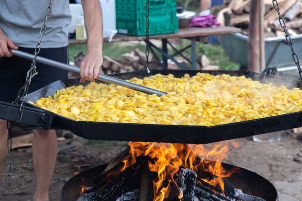 Festival de rue de pommes de terre en Allemagne. Pommes de terre frites traditionnelles avec des oignons sur un feu ouvert dans une énorme poêle. Un homme remue des pommes de terre
. - Photo, image
