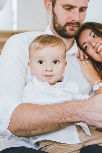 Lindo bebé niño en camisa blanca con su familia feliz en el interior brillante, retrato de cerca
 - Foto, Imagen