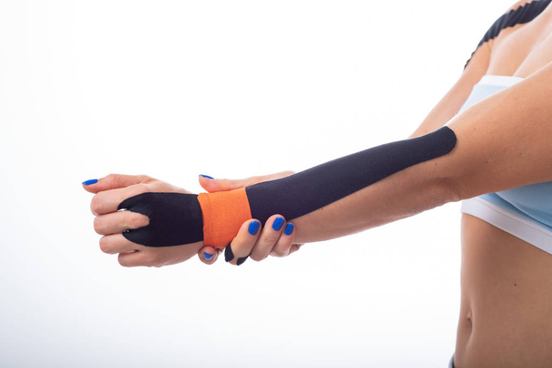 A female athlete puts a kineziotape on her wrist. Kineziology, alternative treatment for injuries of joints and tendons. Physiotherapy of chronic inflammation of the joints of a womans arm. - Fotografie, Obrázek