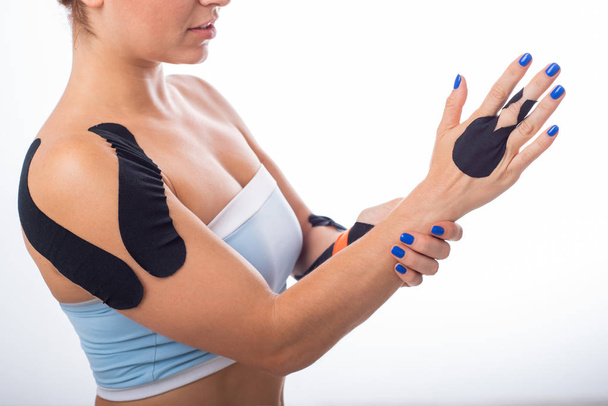 Female shoulder with kineziotape on a white background. Alternative medicine for sports injuries of joints and ligaments. Sportswoman with a black medical record on a sore shoulder and middle finger. - Zdjęcie, obraz