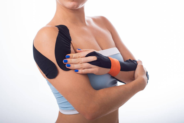 Female shoulder with kineziotape on a white background. Alternative medicine for sports injuries of joints and ligaments. Young sportswoman with medical record on a sore shoulder and wrist. - Valokuva, kuva