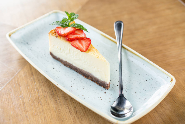 Stukje heerlijke Cheesecake met aardbei en muntblaadjes op wit bord. - Foto, afbeelding
