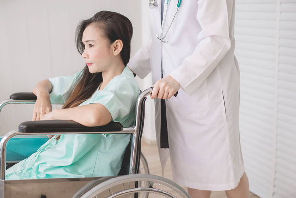 Patientin mit Lähmung sitzt im Rollstuhl, Arzt steht hinter ihr, Gesundheitskonzept - Foto, Bild