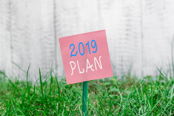 2019年計画を示すメモを書く。今年の目標と計画を設定するビジネス写真、または2019年に貼り付けられ、草原に置かれた普通の紙. - 写真・画像