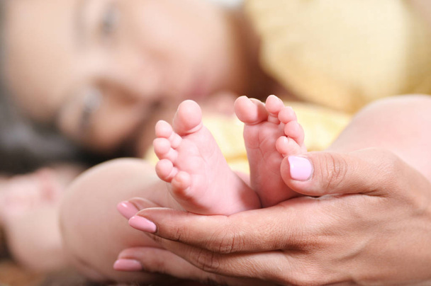 小さな赤ちゃんの足を持つ母親の手のクローズアップ撮影。親の思いやり小さな赤ちゃん - 写真・画像