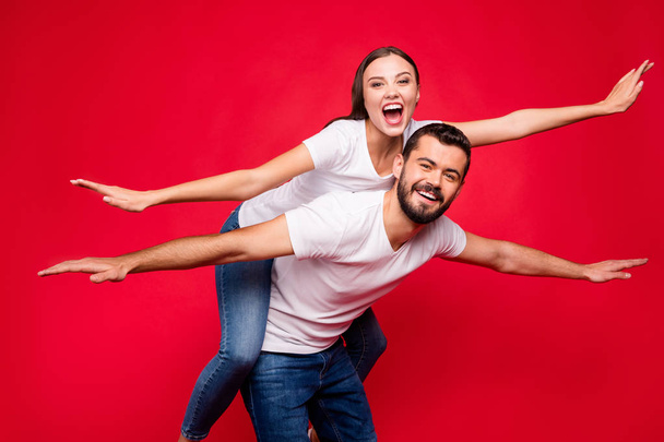 Photo of charming trendy casual cute nice beautiful couple of two people wearing jeans denim white t-shirt piggyback to be flying away abroad while isolated with red background - Foto, Bild